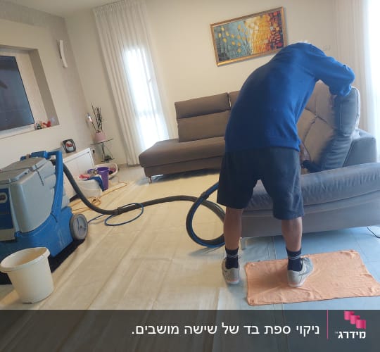 אדם מנקה ספה עם מכונת ניקוי ושואב אבק